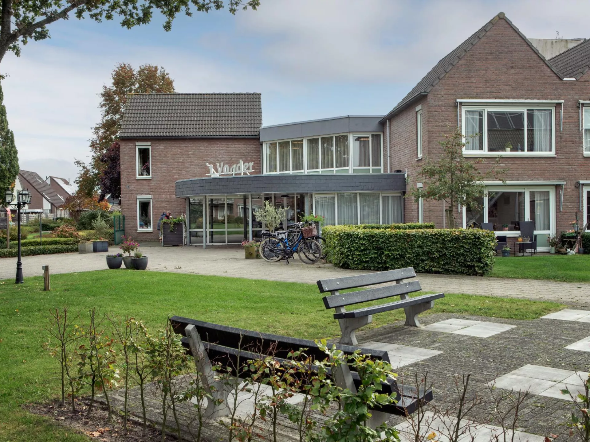 Vooraanzicht van 't Vonder omringd door een tuin en bankjes.