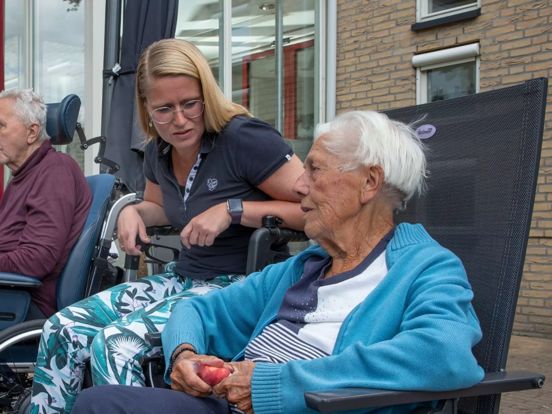 Ouderen en verzorgers zitten buiten te praten bij een zorginstelling.