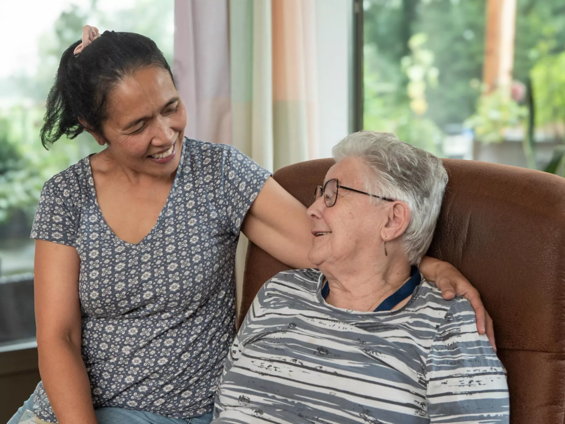 Een zorgzame vrouw omarmt liefdevol een oudere vrouw.