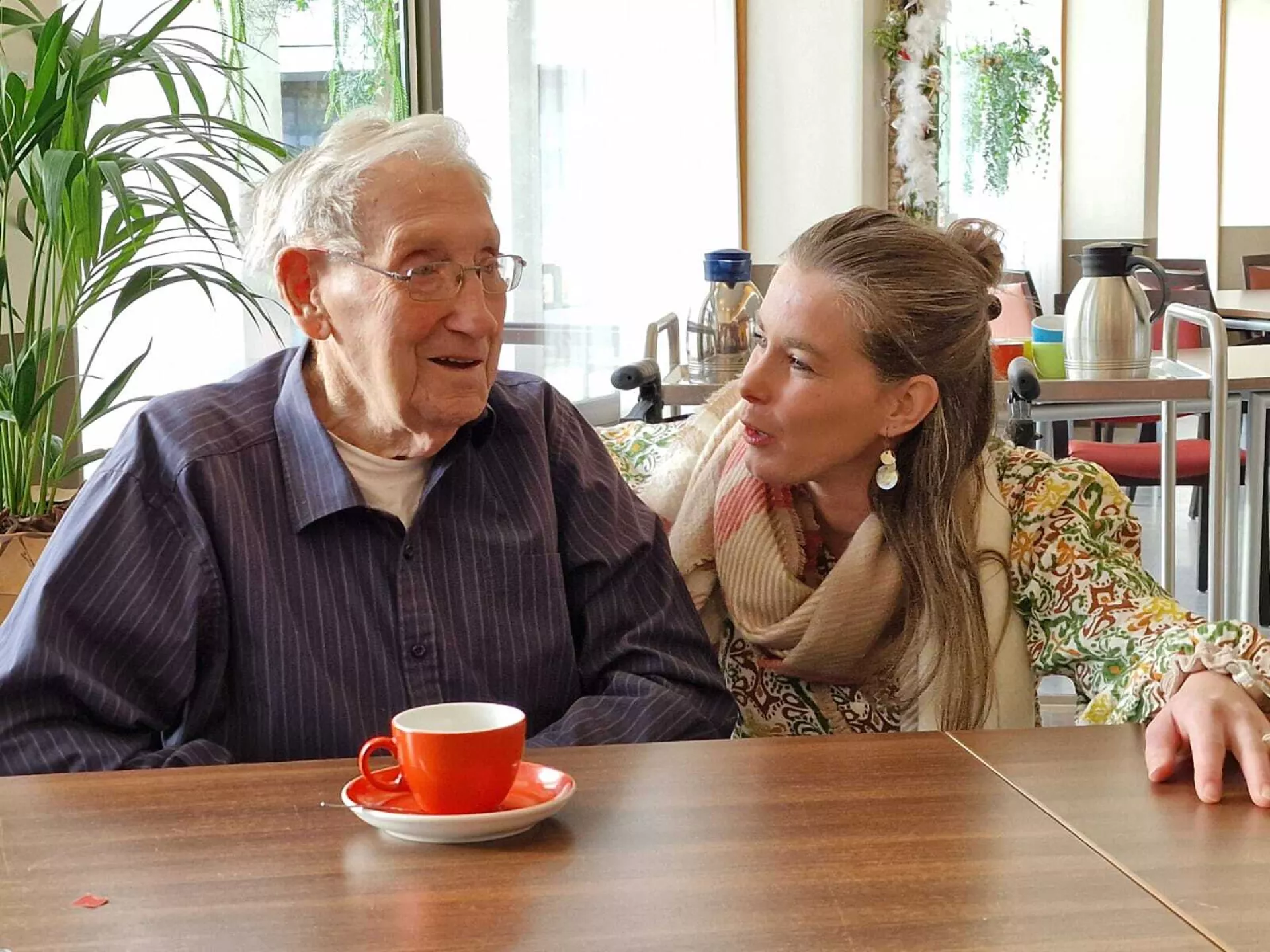 Een oudere man en een vrouw zitten samen aan tafel met koffie.
