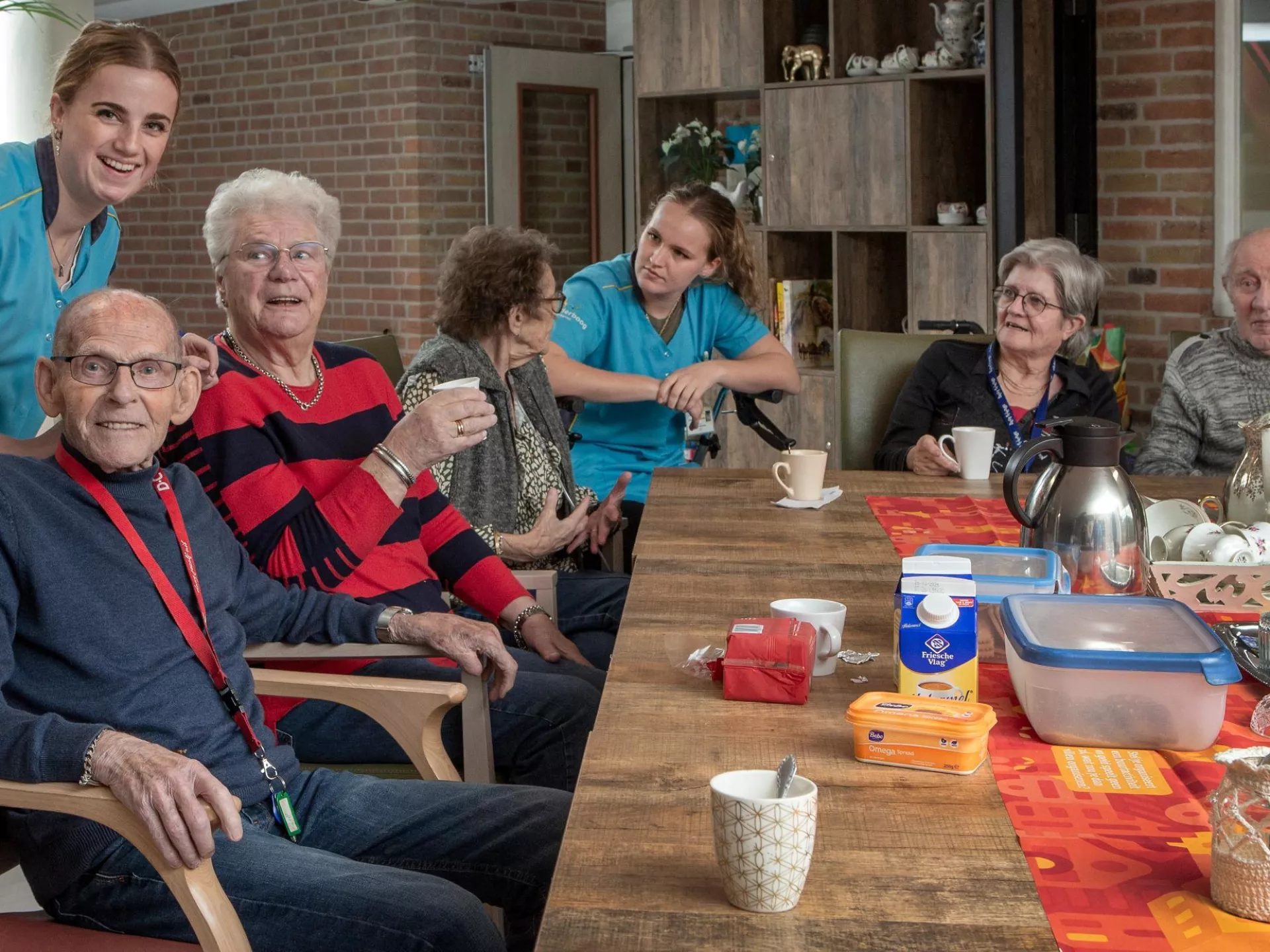 Een groep ouderen en verzorgers aan tafel voor een gezellige samenkomst.