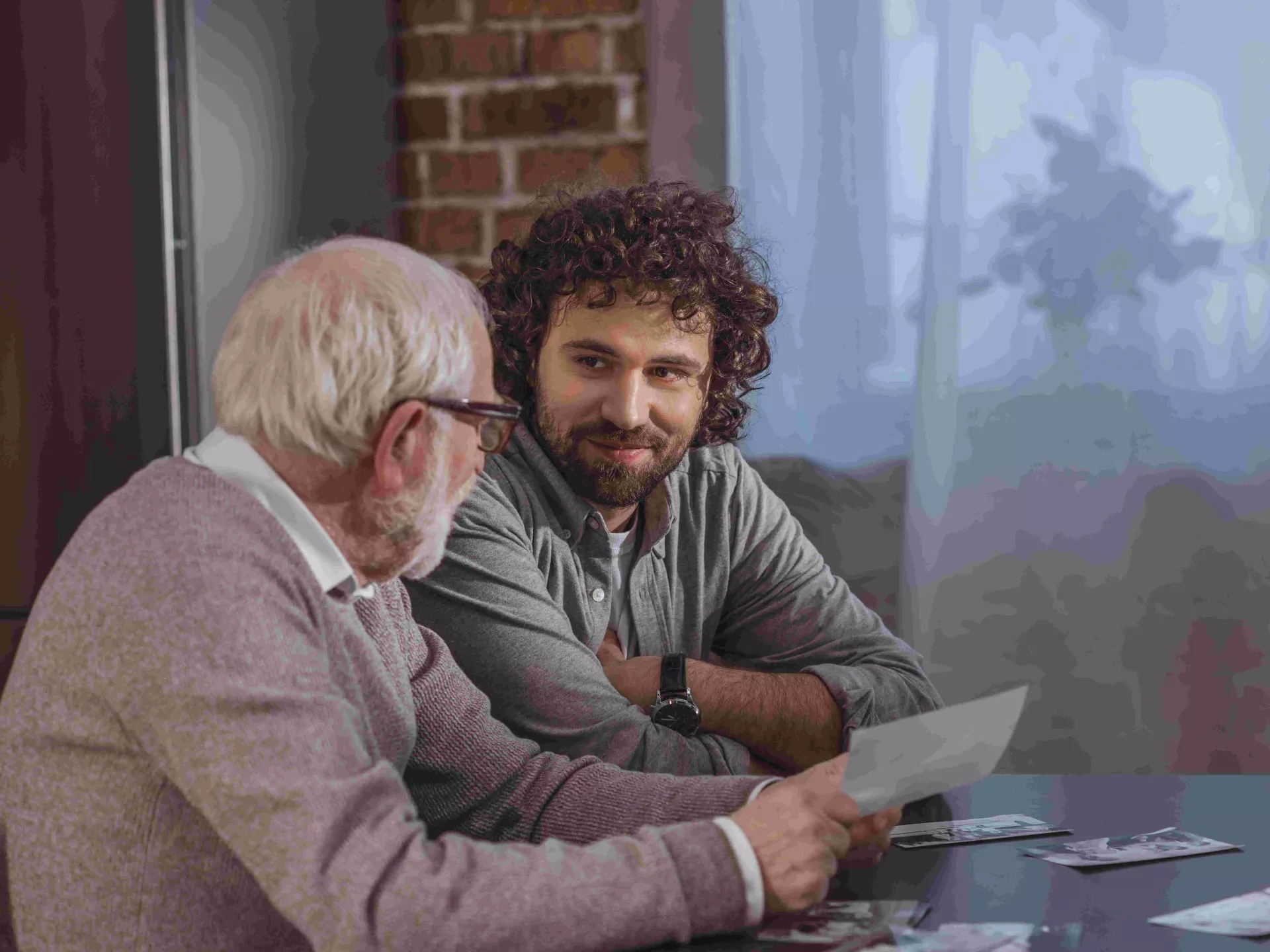 Twee mannen die elkaars gezelschap koesteren terwijl ze aan tafel zitten en naar foto's kijken.