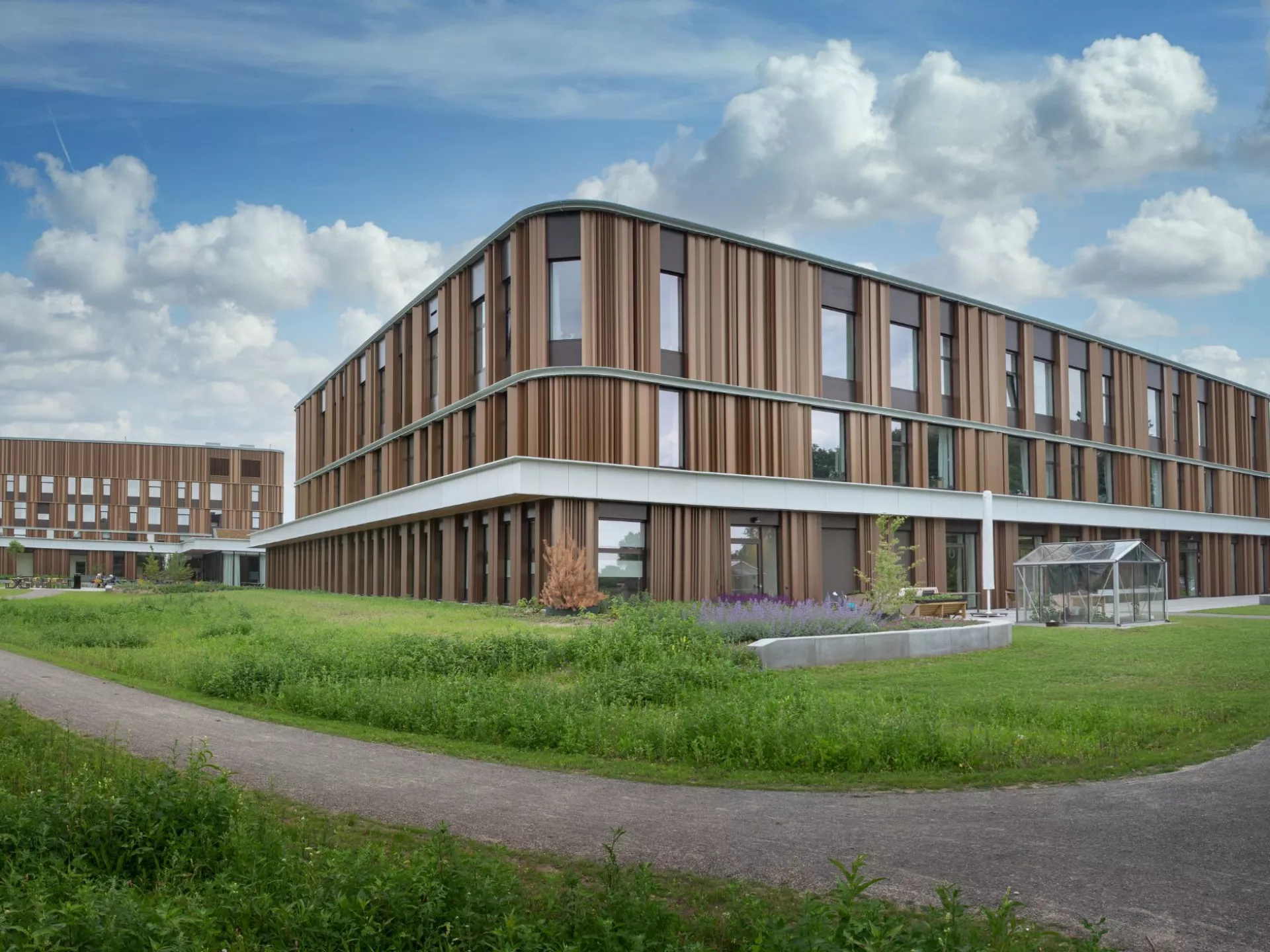 Modern gebouw omgeven door groene velden en paden.