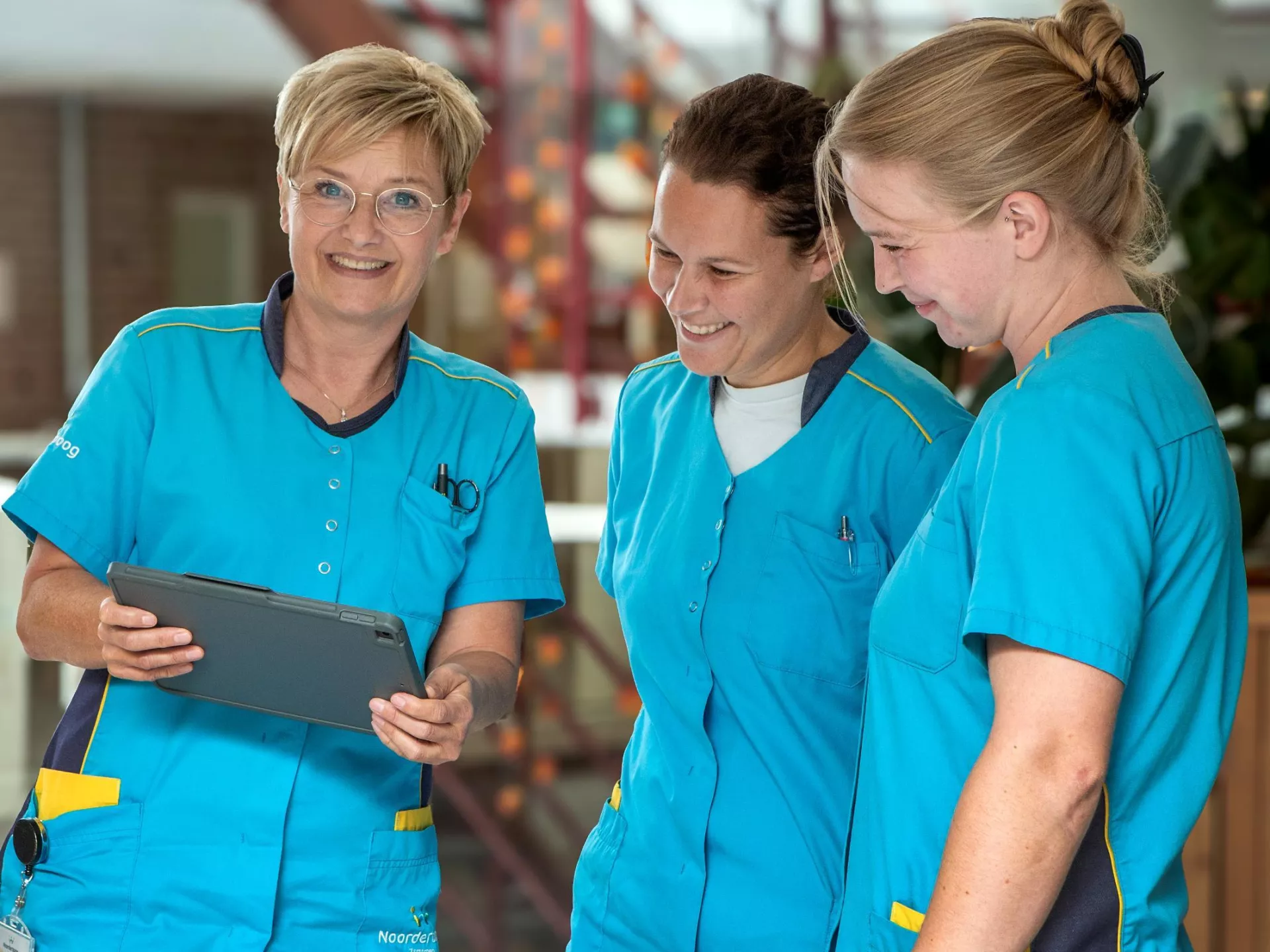 Drie verpleegkundigen in blauwe uniformen bekijken samen een tablet.
