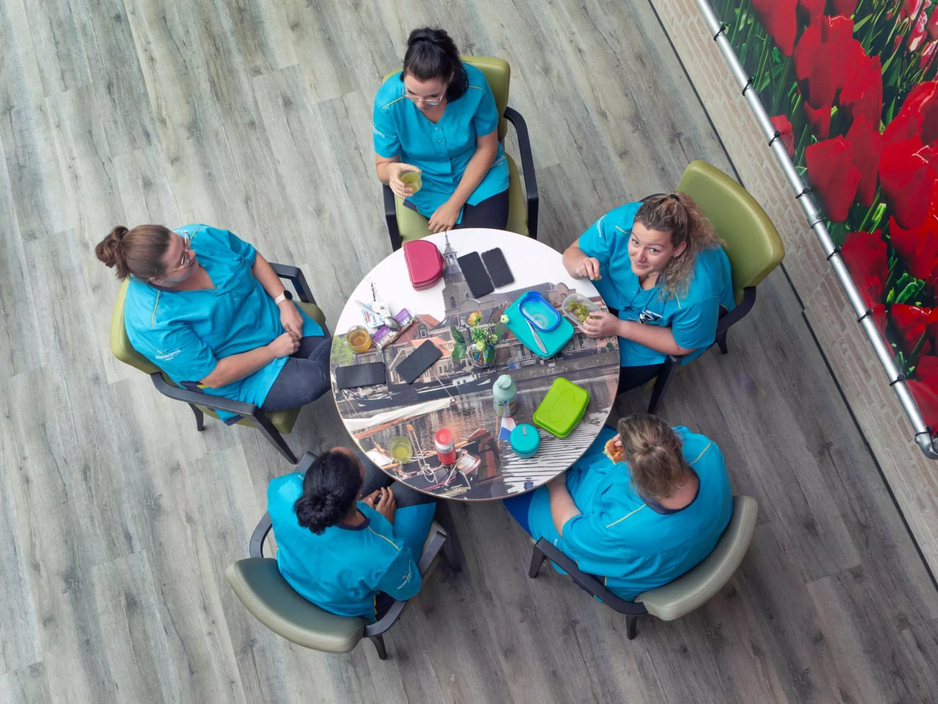 Medewerkers in blauwe zorgjasjes rond een tafel bij een pauze.