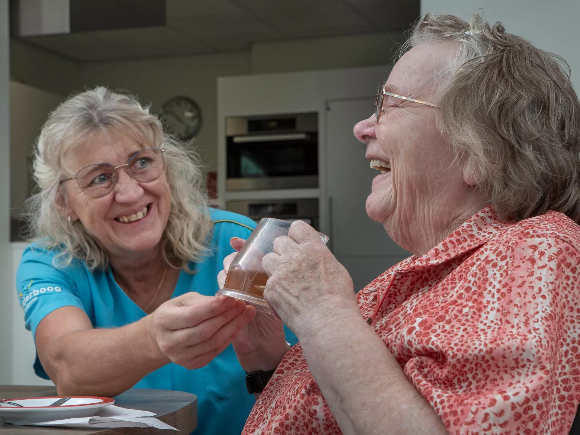 Een verzorgende vrouw helpt een oudere dame met het drinken.