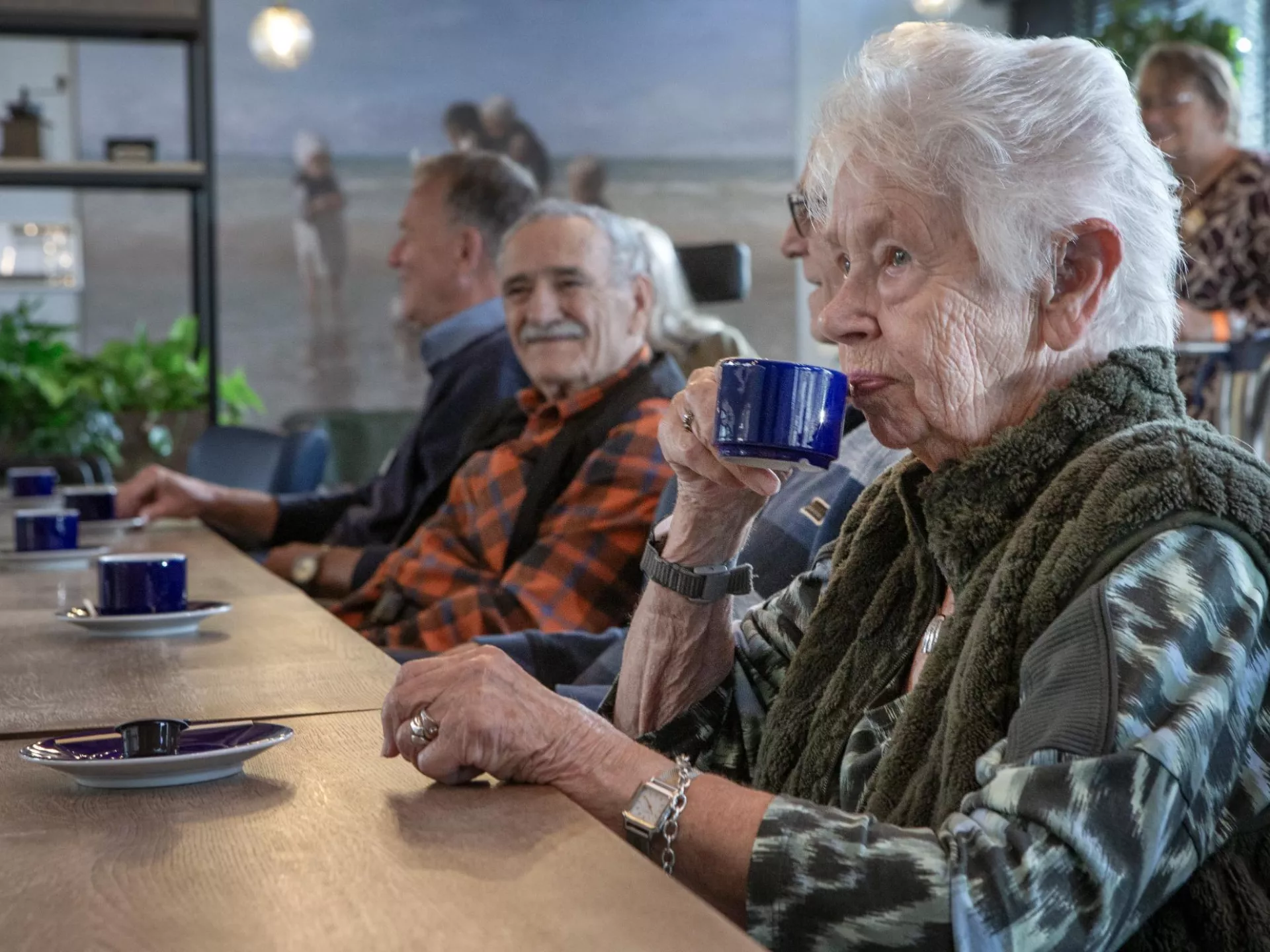 Ouderen drinken koffie en kletsen aan een tafel.