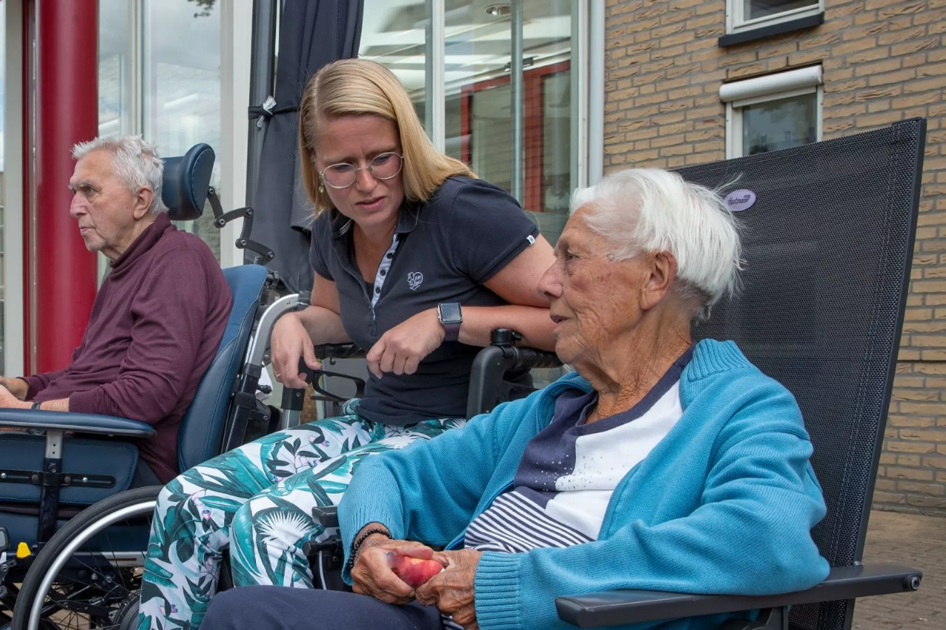 Ouderen en verzorgers zitten buiten te praten bij een zorginstelling.