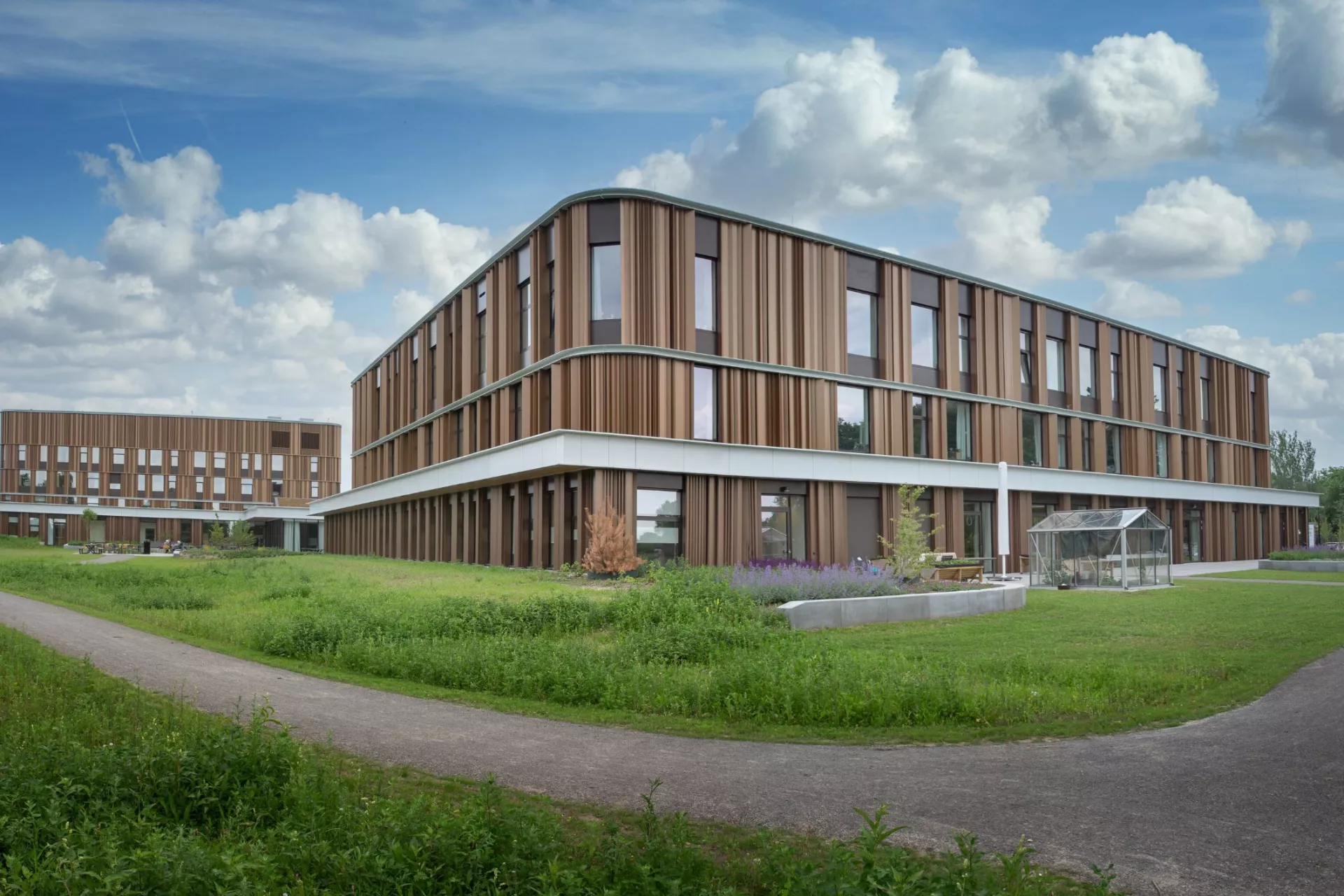 Modern gebouw omgeven door groene velden en paden.