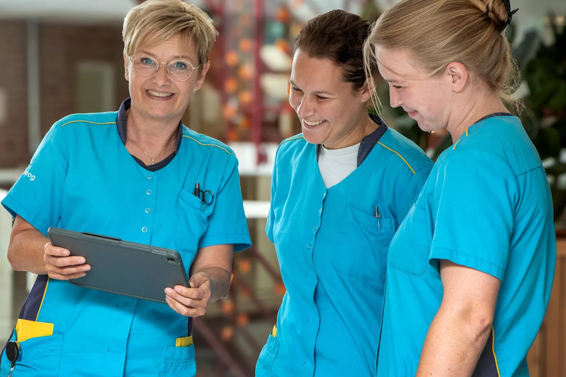 Drie verpleegkundigen in blauwe uniformen bekijken samen een tablet.