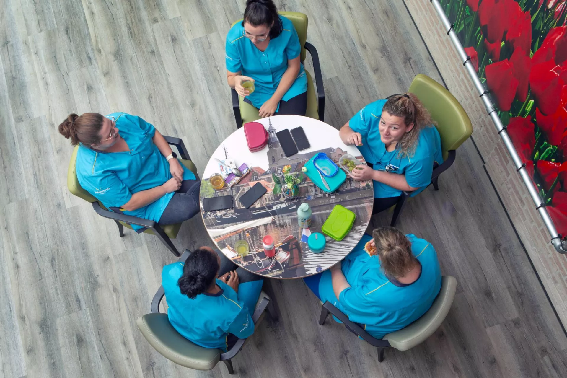 Medewerkers in blauwe zorgjasjes rond een tafel bij een pauze.